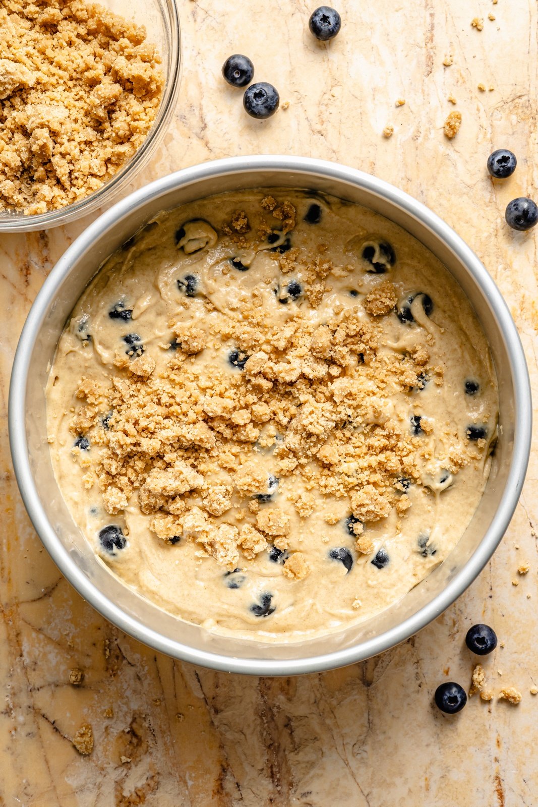 adding a streusel topping to unbaked blueberry coffee cake