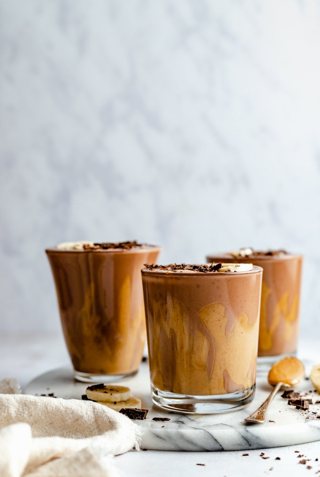 three chocolate peanut butter banana smoothies on a marble board
