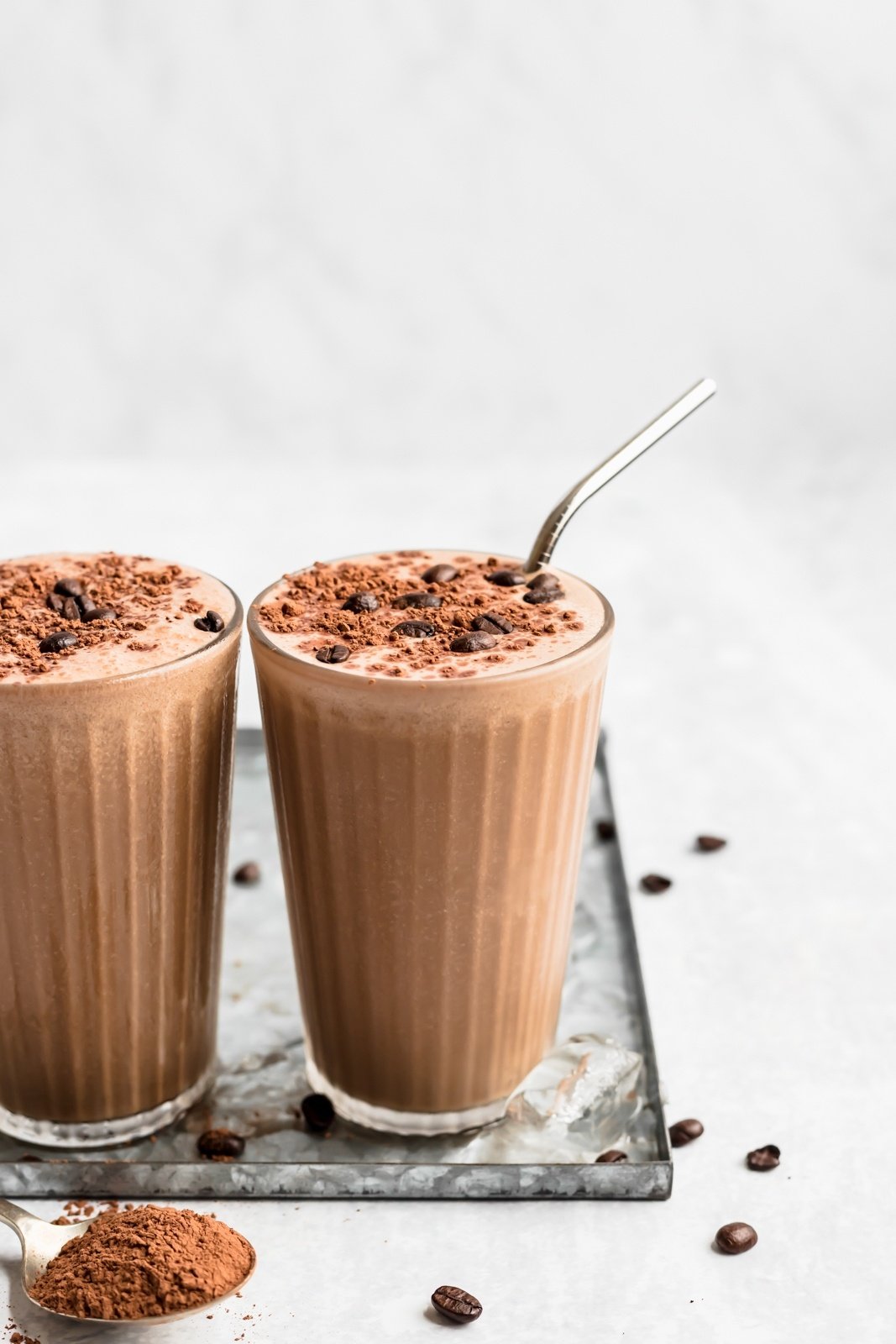 two coffee smoothies in glasses topped with cacao powder