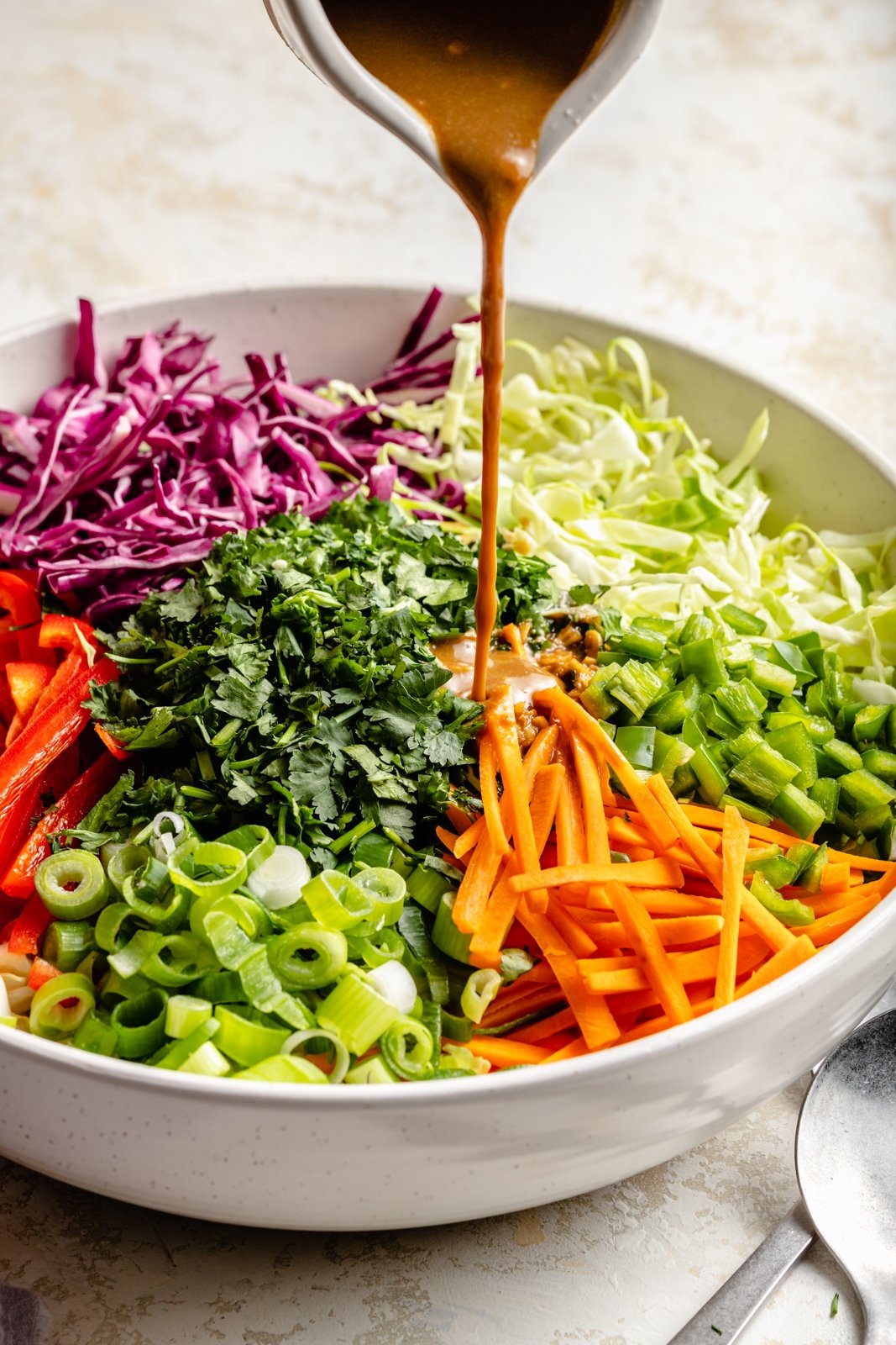pouring dressing into a sesame chicken salad in a bowl