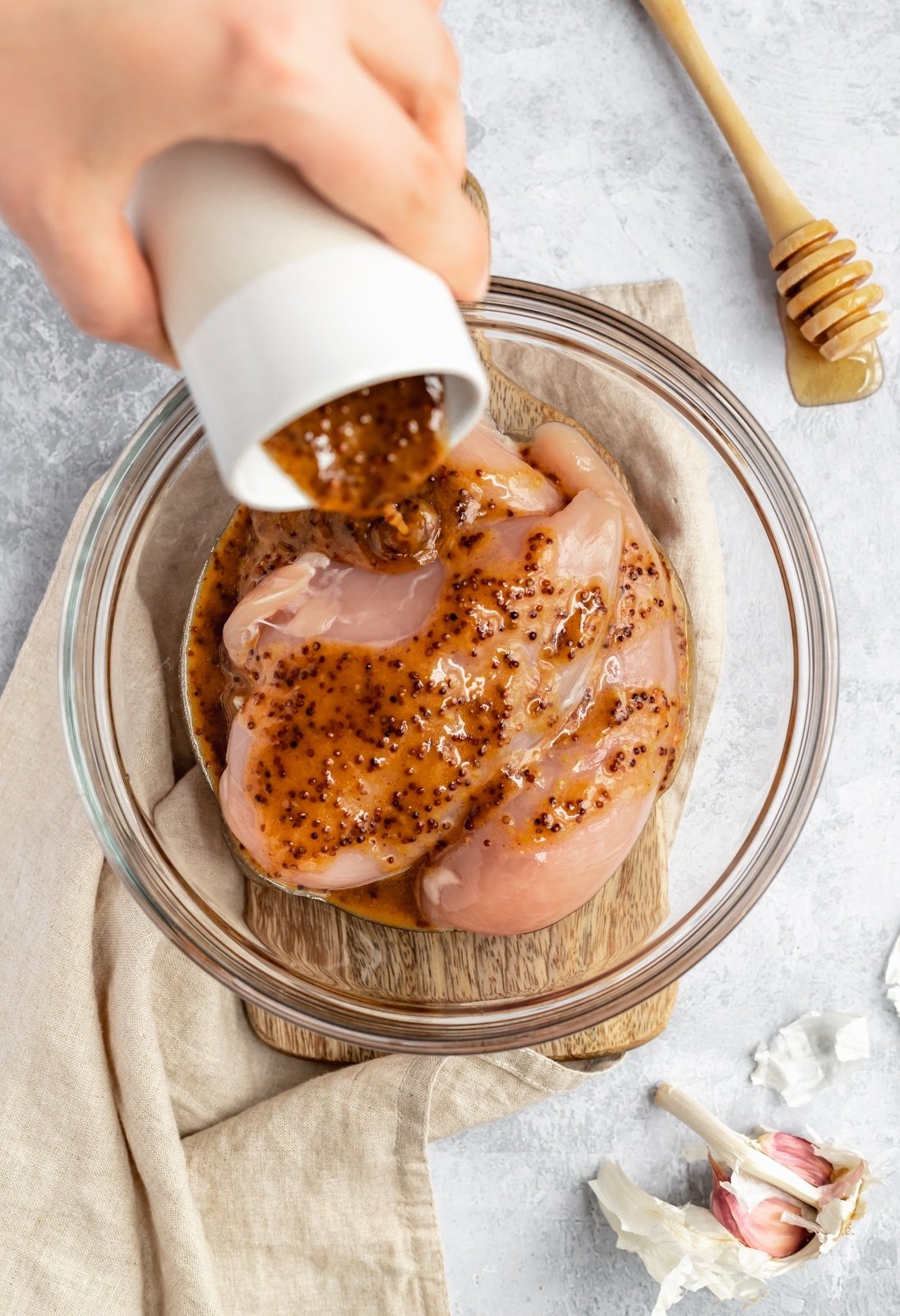 pouring paleo honey mustard marinade into a bowl of chicken