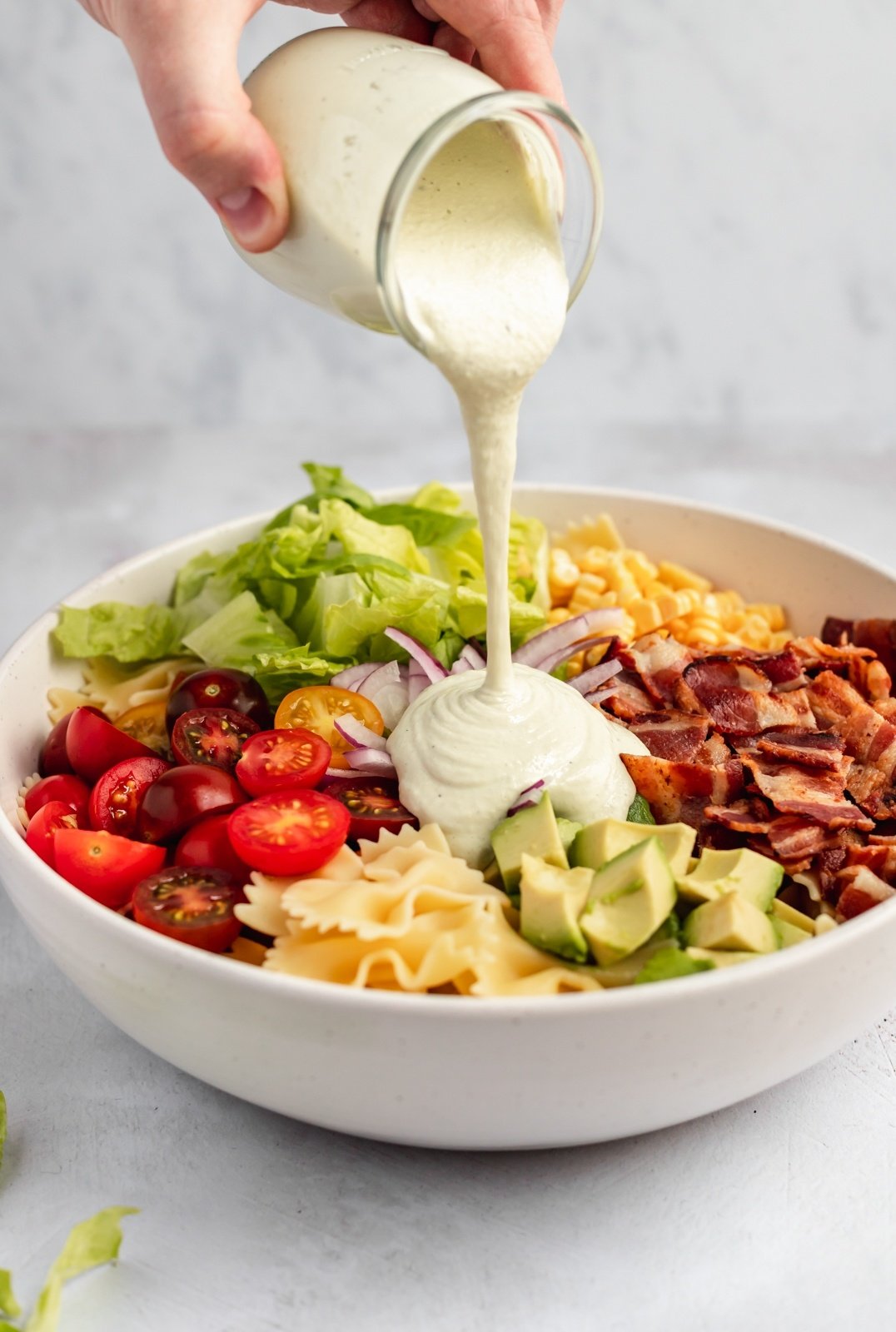 pouring cashew dressing into a BLT pasta salad