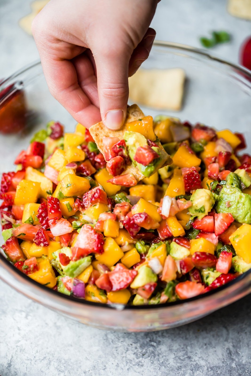 dipping a pita chip into strawberry mango salsa with avocado in a glass bowl