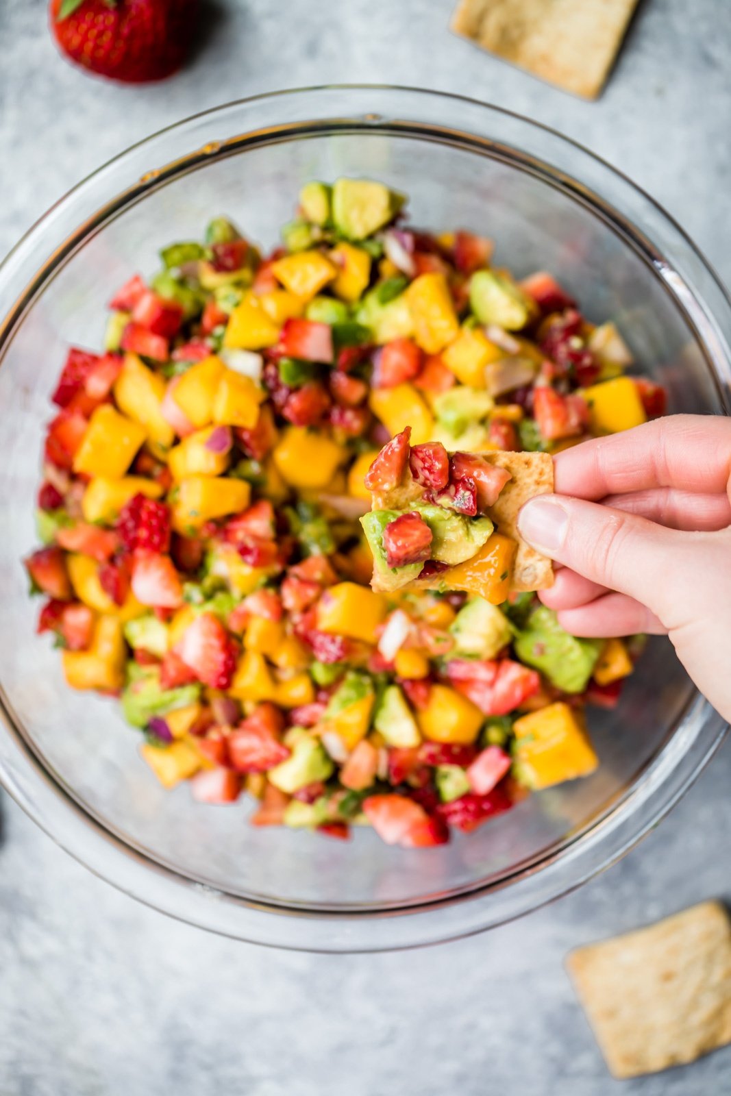 dipping a chip into Avocado Strawberry Mango Salsa in a glass bowl