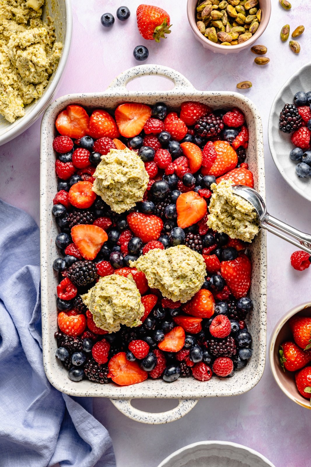 scooping dough on top of a berry cobbler in a pan