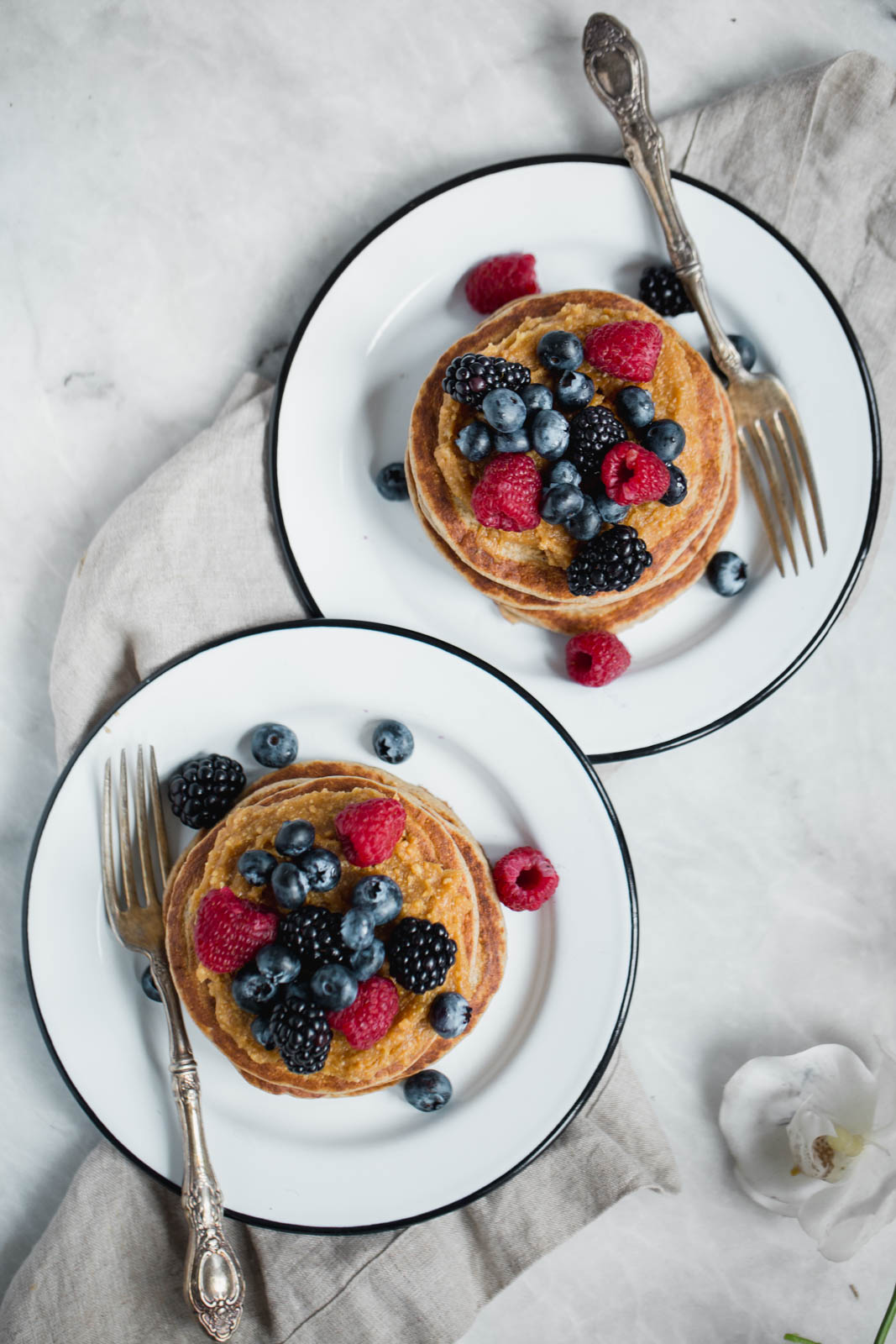 two stacks of cottage cheese protein pancakes on two plates topped with berries
