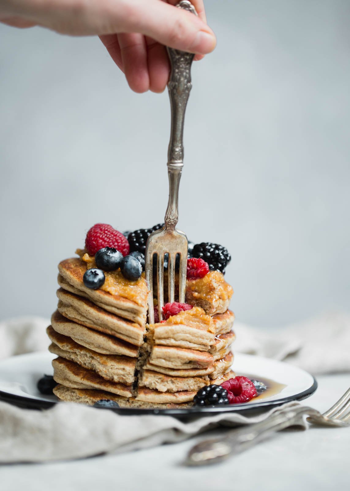 fork sticking into cottage cheese pancakes topped with berries on a plate