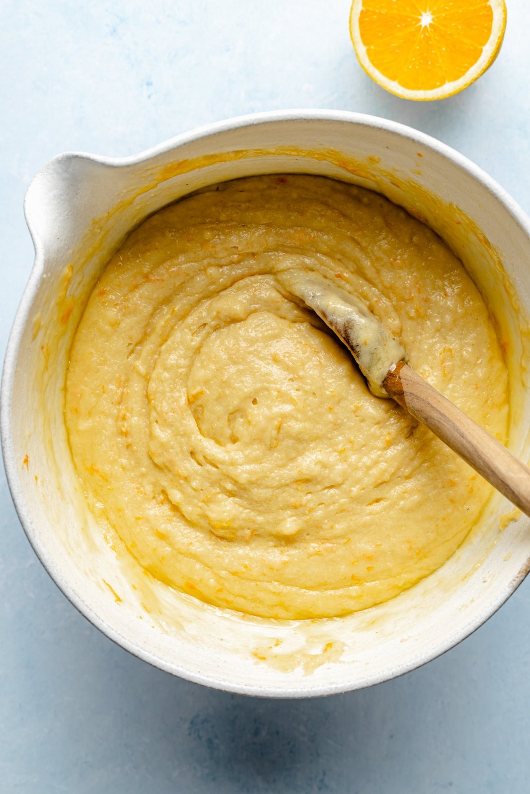 batter for bakery-style orange muffins in a bowl with a wooden spoon