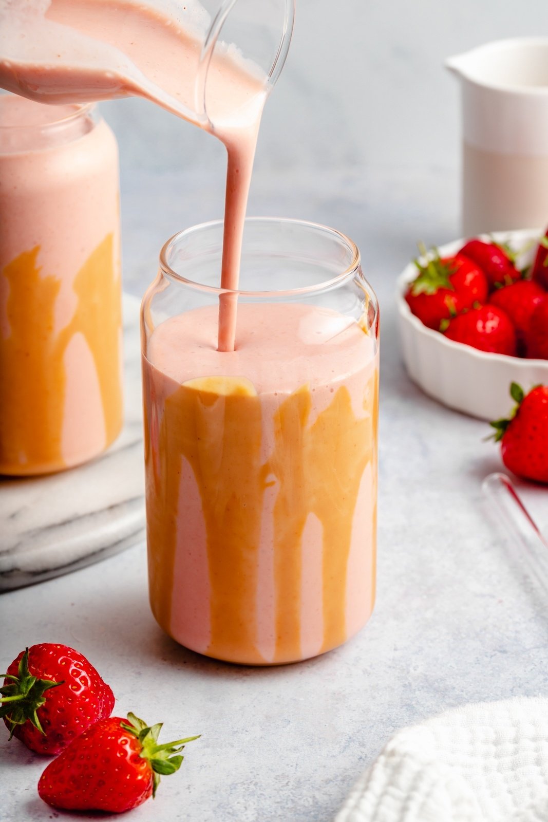 pouring a vegan peanut butter strawberry banana smoothie into a glass