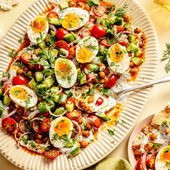 spiced chickpeas and eggs with cucumber salad and yogurt on a platter