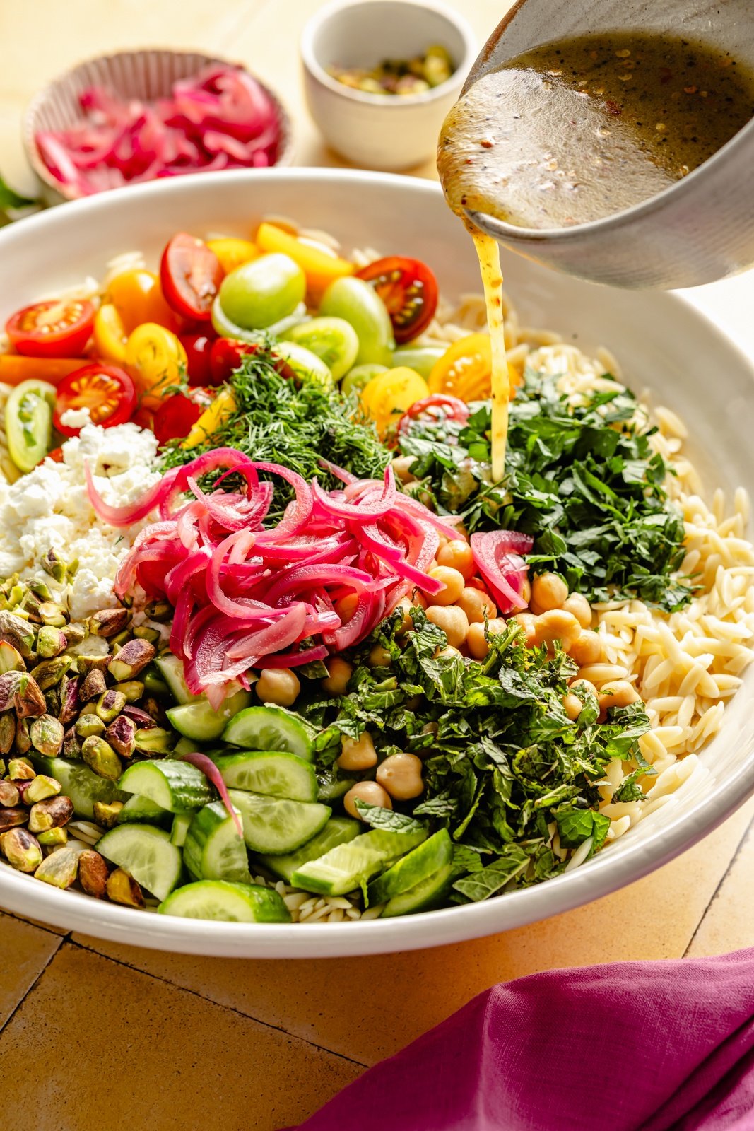 pouring dressing over an herby chickpea feta pasta salad in a bowl